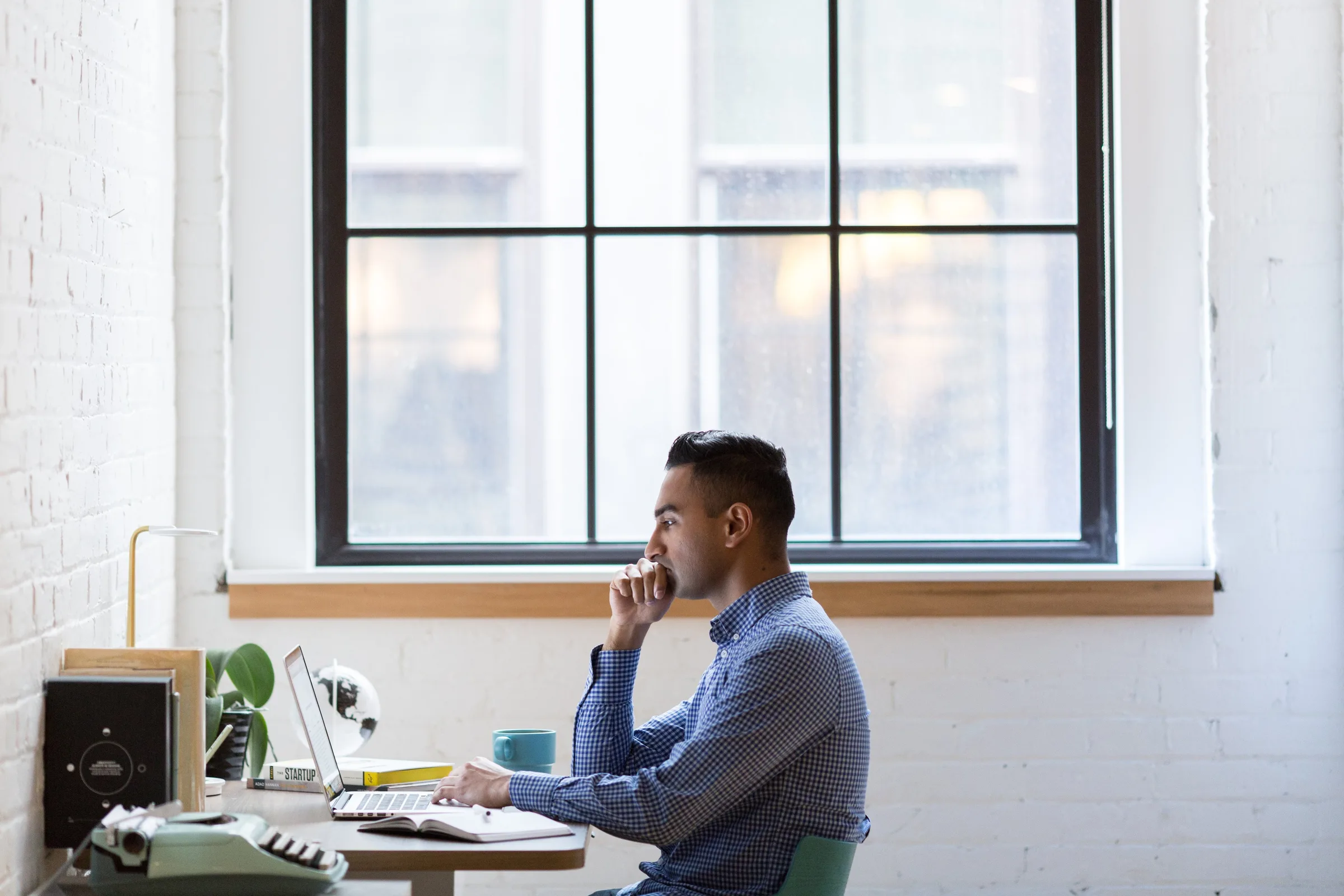 A man thinking at his desk by a tall office window