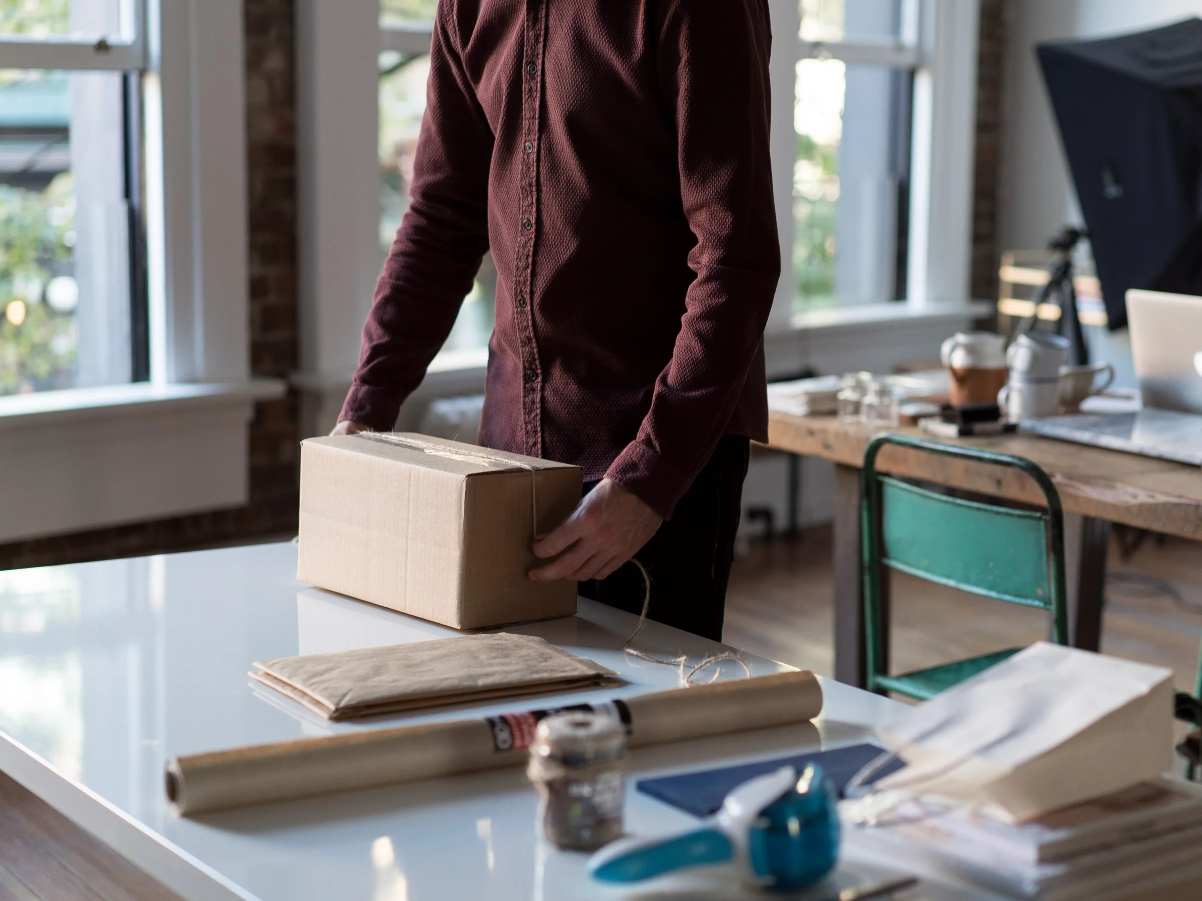 A person packing an order into a cardboard box at a bright office desk