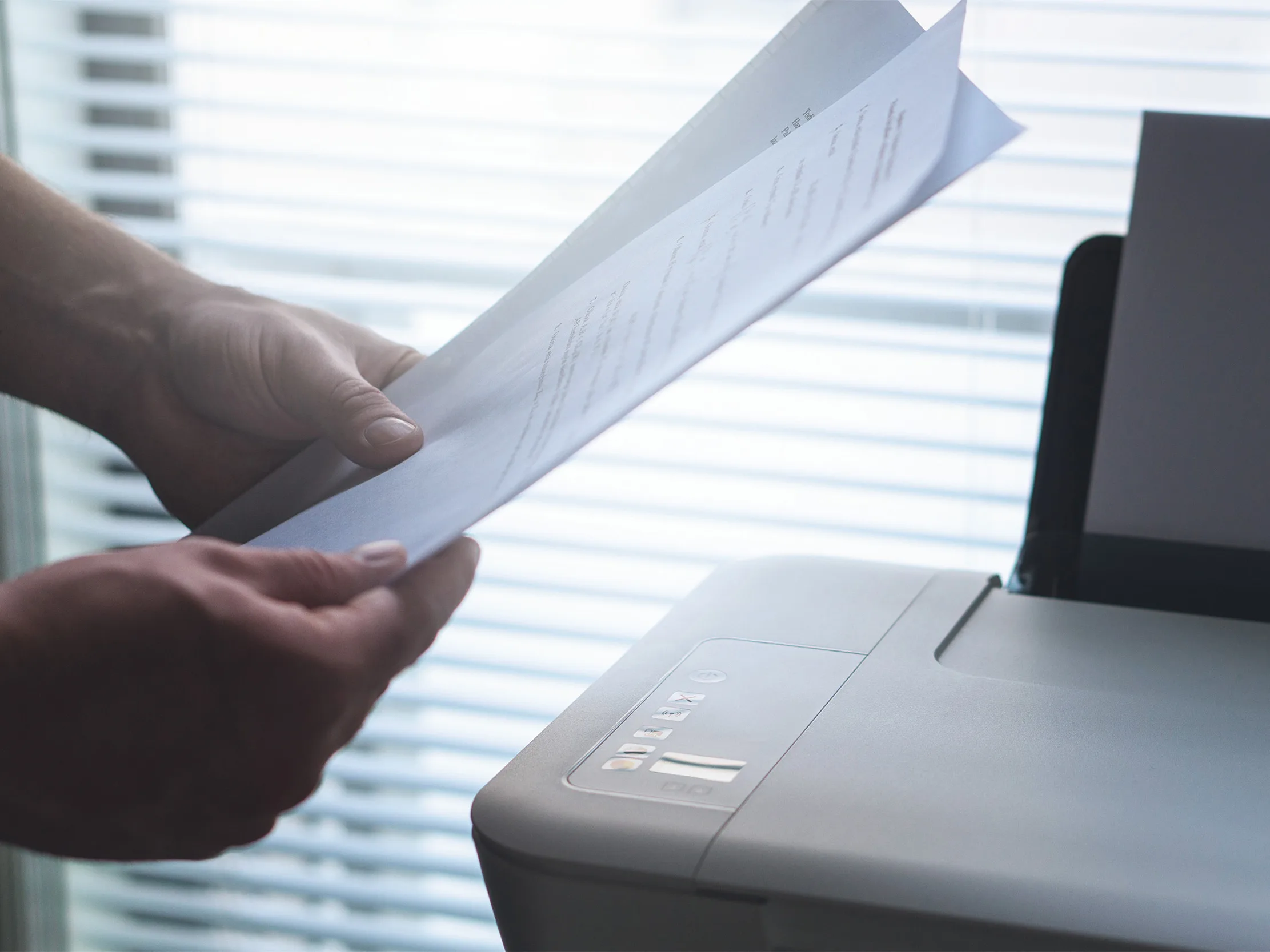 A person reading a printed report next to the office printer