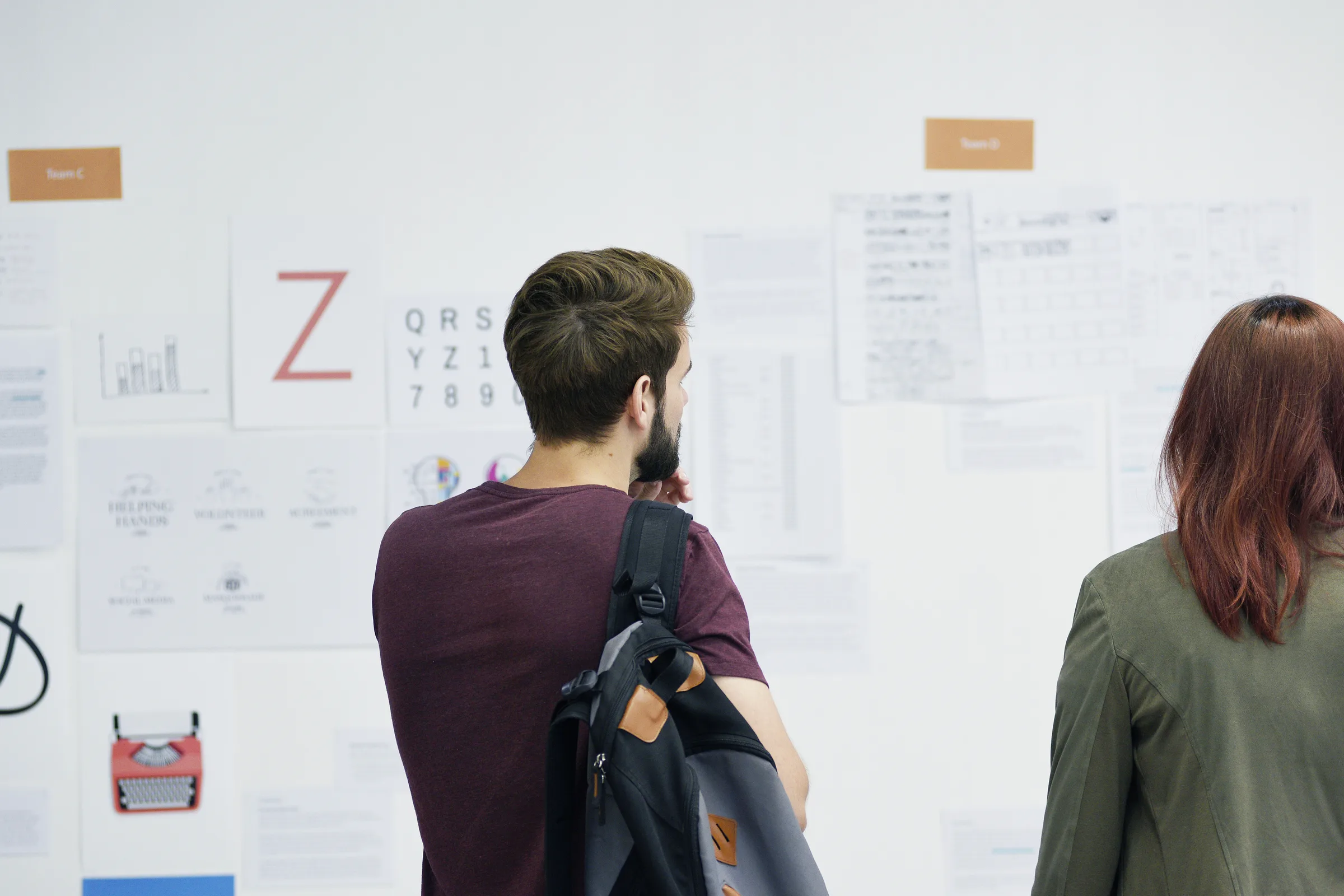 Two colleagues reviewing printed plans pinned to a wall