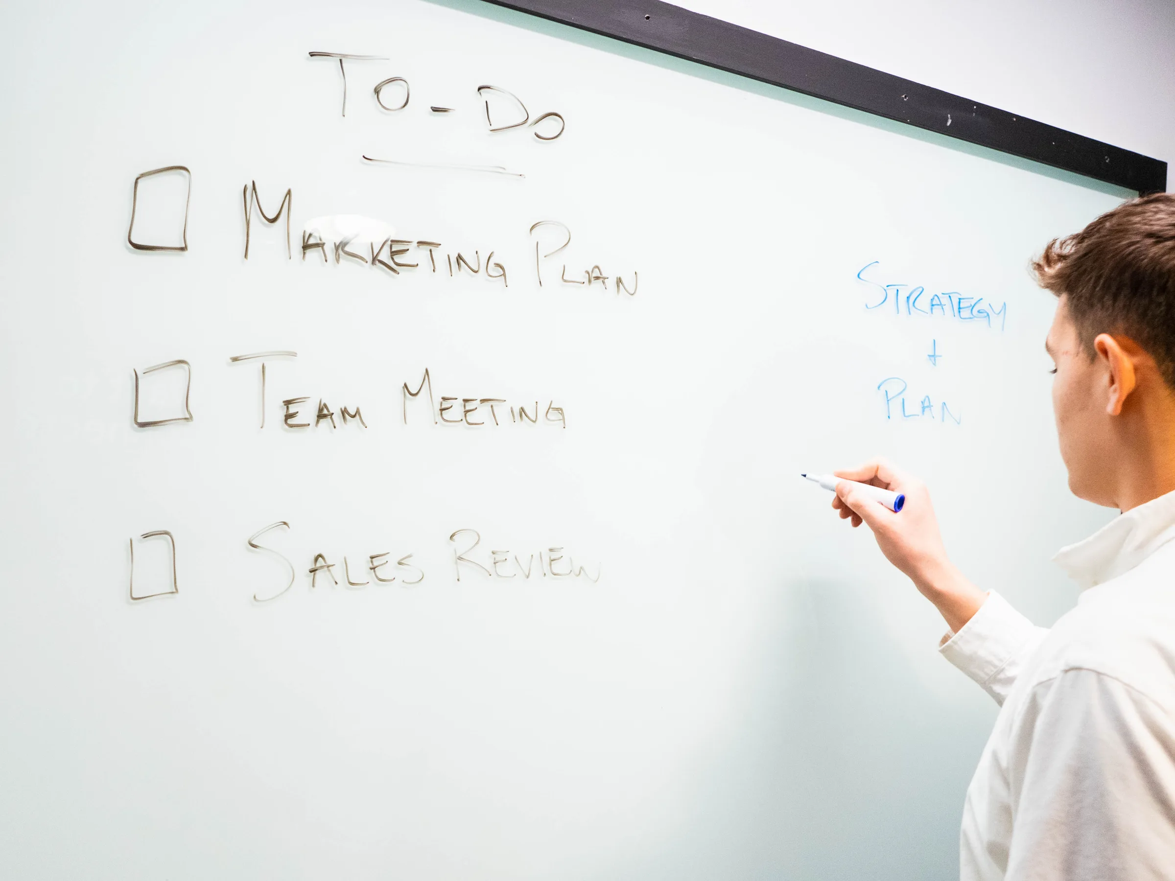 A man writing the next steps of a to-do list on an office whiteboard