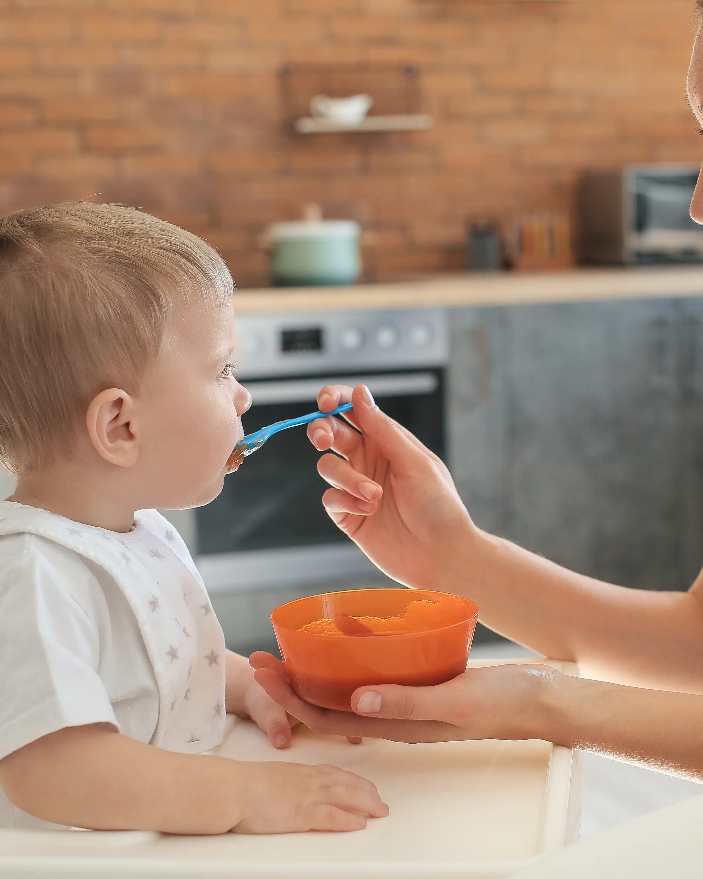 A mother feeding her toddler in a home kitchen