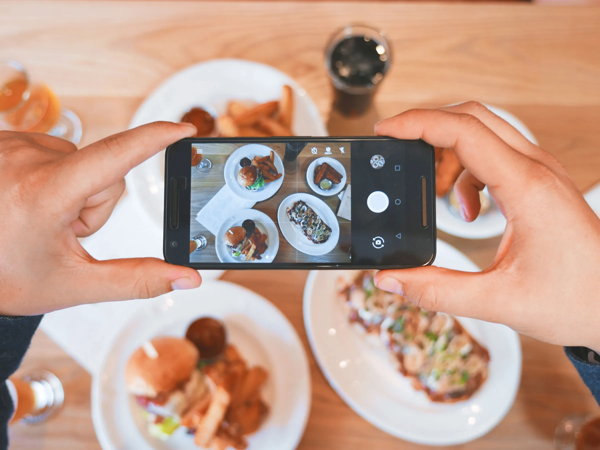 Hands filming plates of food on a cafe table with a phone