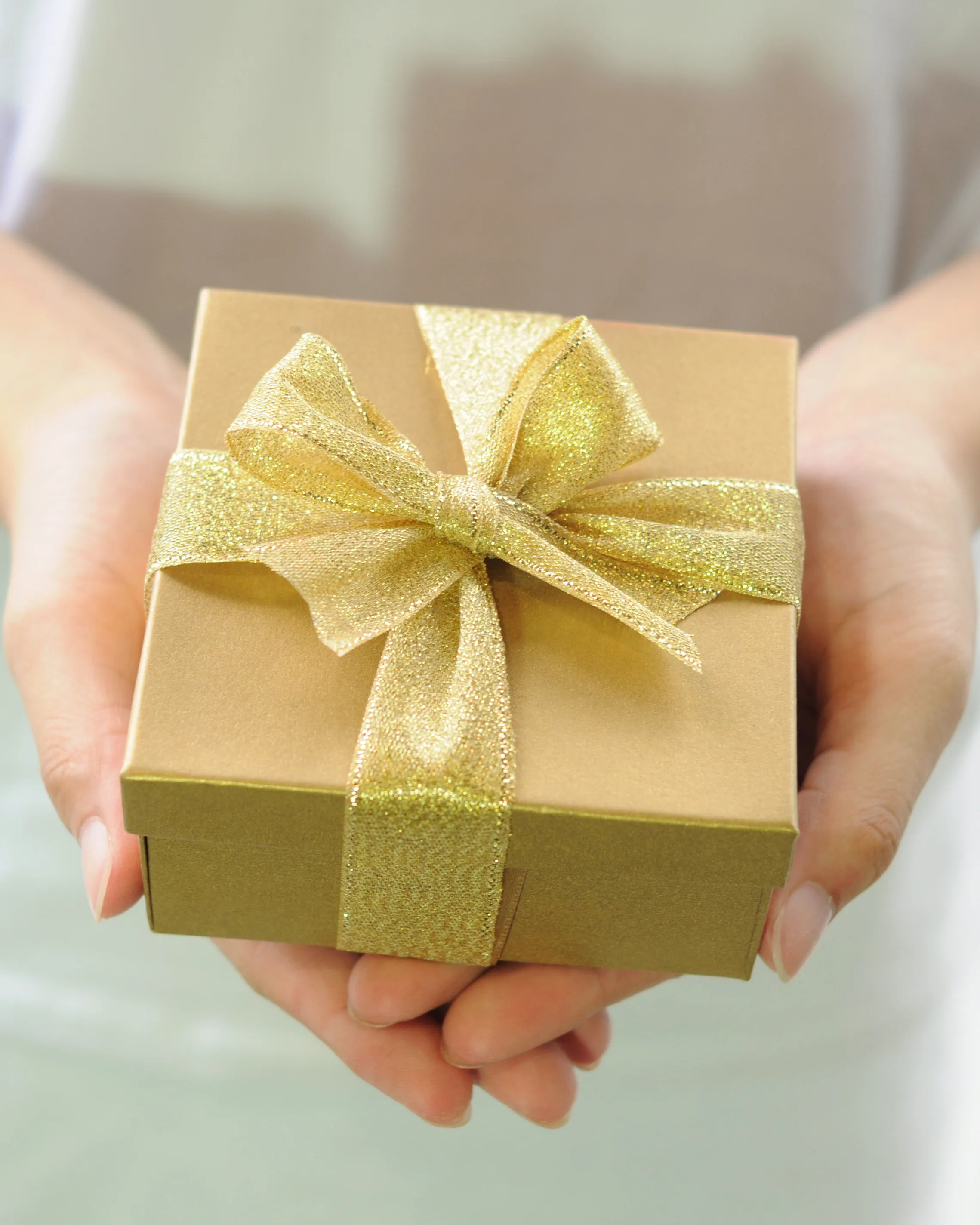 Hands holding out a small box tied with a gold ribbon